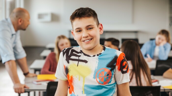 © Philipp Lipiarski Schüler sitzt lächelnd in der Klasse und blickt in Richtung Kamera