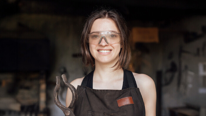 Junge Frau mit Schutzbrille erlernt das Schmiedehandwerk
