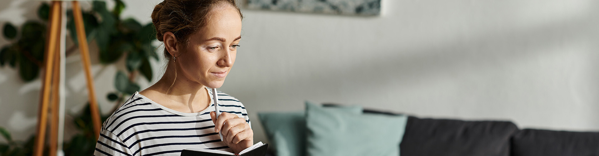 Frau schaut nachdenklich nach unten in einen Laptop, h&auml;lt ihren Stift unters Kinn