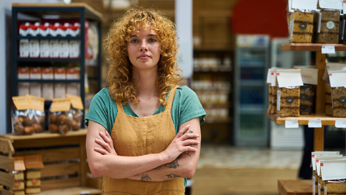 © alvaro, stock.adobe.com Selbstbewusste Verkäuferin steht mit verschränkten Armen im Supermarkt.