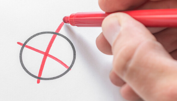Hand zeichnet mit einem roten Filzstift ein Kreuz in einen Kreis