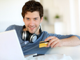 Mann sitzt vor einem Laptop und hält eine Kreditkarte in der Hand