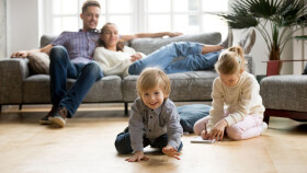 Kinder spielen am Boden während Eltern vom Sofa aus zusehen