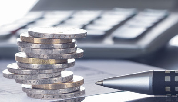 Auf einem Tisch liegt ein Formular, darauf steht im Hintergrund ein Tischrechner, im Vordergrund liegt ein M&uuml;nzstapel und  ein Kugelschreiber