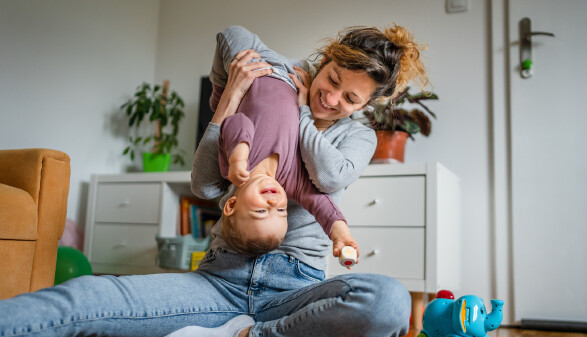 Mutter h&auml;lt ihr lachendes Kleinkind kopf&uuml;ber in die Luft