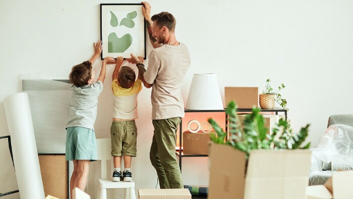 © Seventyfour, stock.adobe.com Papa und Söhne hängen ein Bild in der neuen Wohnung auf