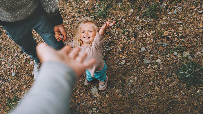 Ein kleines Mädchen geht mit Vater und Mutter im Freien spazieren.