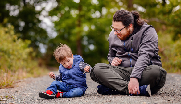 Vater sitzt mit seinem spielenden Kleinkind auf einem Spazierweg im Wald