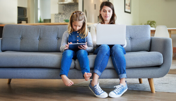 Mama mit Laptop und Kind mit Tablet sitzen auf dem Sofa.