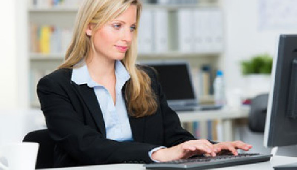 Eine Frau im Anzug sitzt am Schreibtisch und blickt auf den Computerbildschirm vor sich. Im Hintergrund sieht man ein Regal mit Ordnern. © Racle Fotodesign, stock.adobe.com