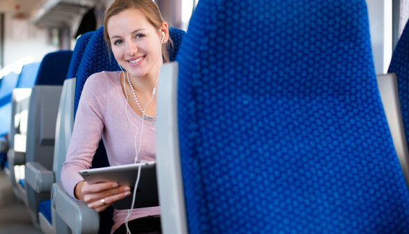 Frau reist mit Tablet in der Hand und Kopfhörern in den Ohren im Zug